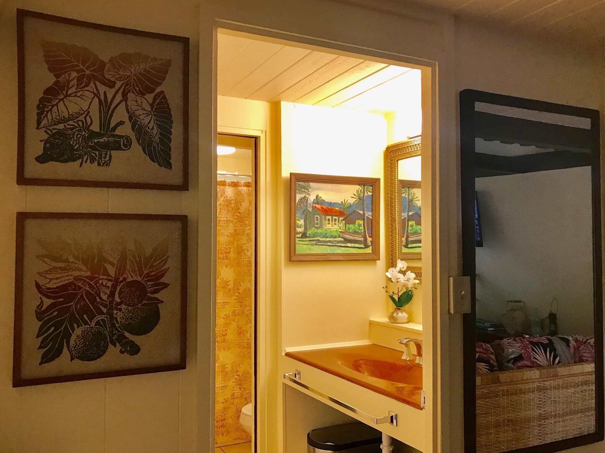 Un baño con un lavamanos de madera, un espejo y dos láminas botánicas enmarcadas en la pared.