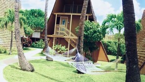 A two-story wooden building with a balcony, surrounded by palm trees and a hammock.