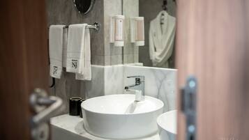A modern bathroom with a round white sink, a mirror, and two towel dispensers.