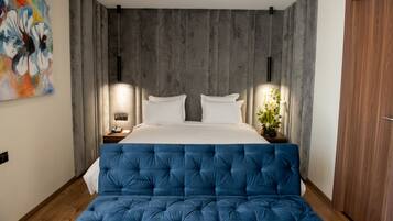 Un dormitorio con una cama grande, un cabecero tapizado azul, un cabecero de madera, una mesita de noche, una lámpara y un cuadro en la pared.