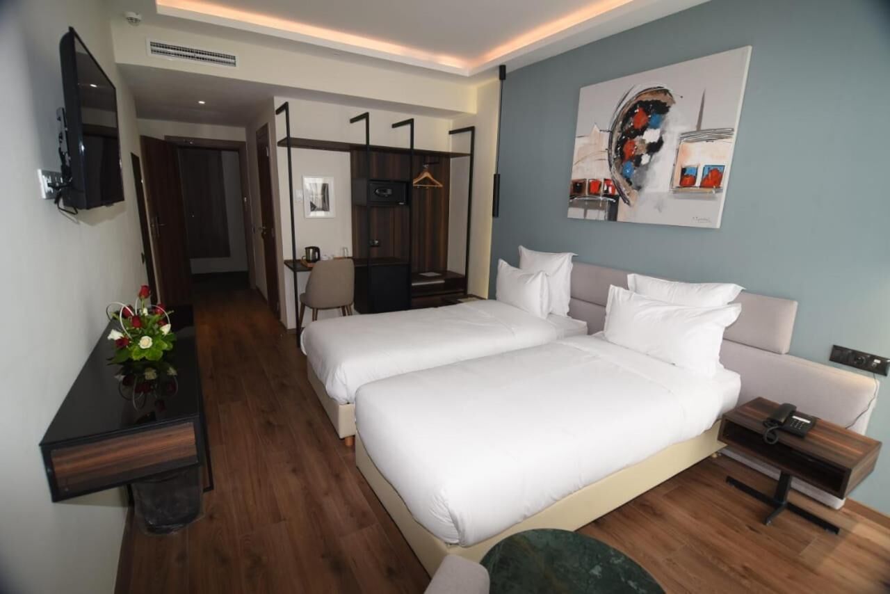 A hotel room with two beds, a desk, a chair, a TV, and a painting on the wall.