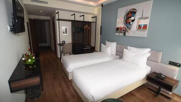A hotel room with two beds, a desk, a chair, a TV, and a painting on the wall.