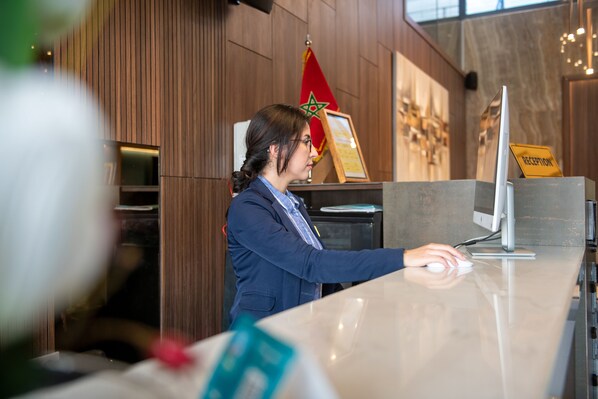 Un mostrador de recepción con un monitor de computadora, una bandera y un letrero de recepción.
