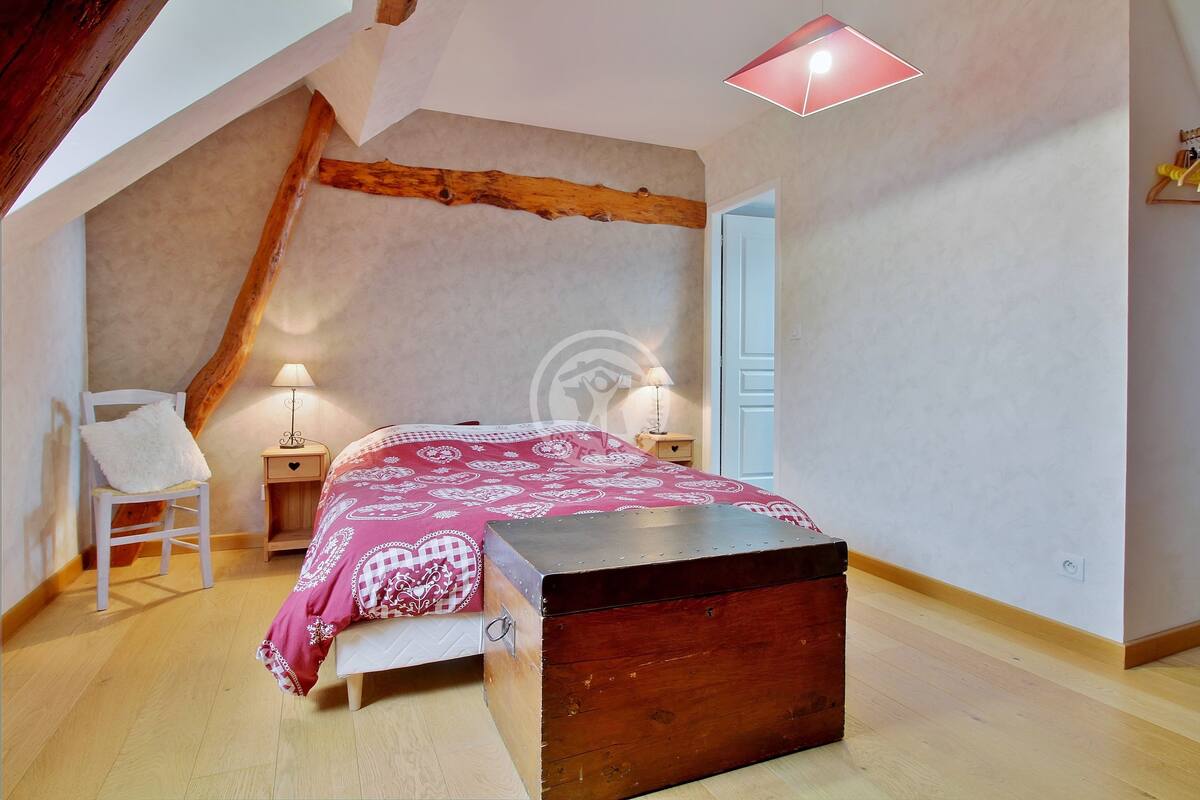 Ein Schlafzimmer mit schrägen W änden, einer Holzbank, einem Bett mit gemustertem Überwurf, zwei Nachttischen mit Lampen und einer Tür zu einem weiteren Raum.
