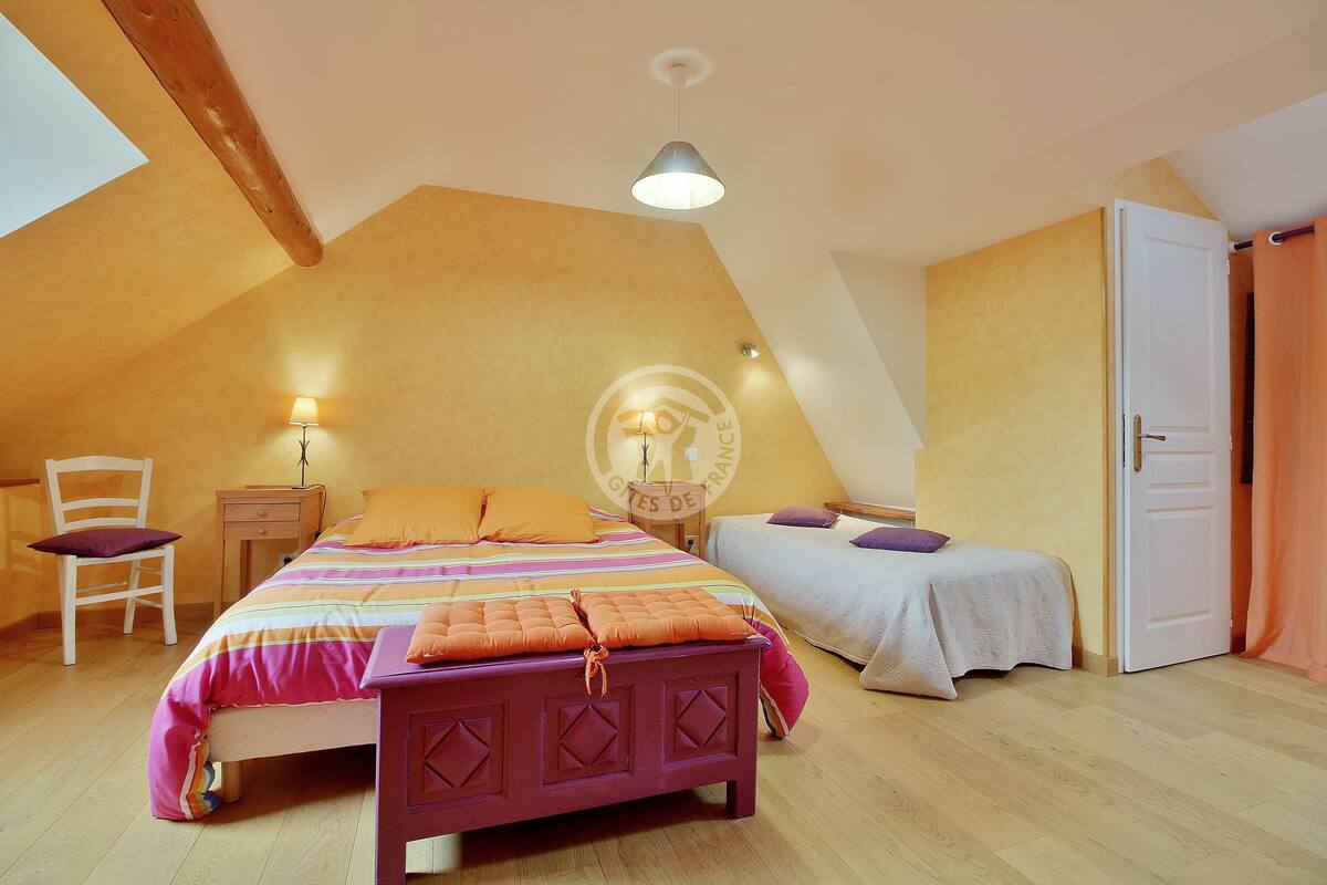 Ein Schlafzimmer mit schrägem Dach, einem Bett mit gestreifter Bettdecke, einem Nachttisch mit Lampe, einem Sessel und einem Kleiderschrank.