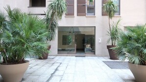 A building entrance with large potted plants, a tiled walkway, and a glass door leading inside. - Lario Apartment (Como)