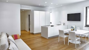 A modern kitchen with white cabinetry, a dining area with a marble table, and a living room with a sofa and a TV. - Lario Apartment (Como)
