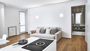 A modern living room with a sofa, a kitchen area with a stove, and a bathroom visible through an open door. - Lario Apartment (Como)