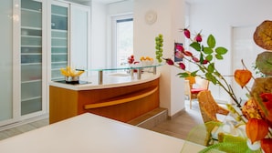 A modern kitchen with a glass-top island, white cabinets, and a dining area with wicker chairs. - Victoria Apartment (Como)