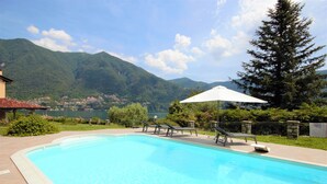 A swimming pool with lounge chairs and an umbrella, surrounded by greenery and mountains in the background. - Villa Oliveto with Pool and Lake view (Laglio)