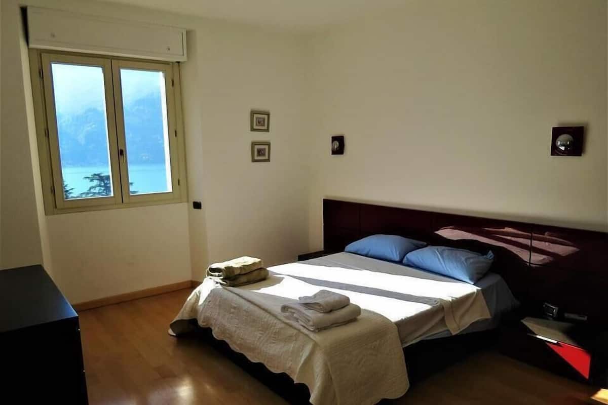 A bedroom with a bed, a window with a view, a bedside table, and a nightstand.
