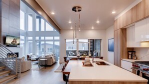 A modern kitchen with a large island, wooden cabinets, and a dining area with a view.