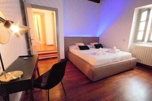 Une chambre à coucher avec un lit, un bureau et une chaise. Il y a une fenêtre et une porte qui donne sur une autre pièce.