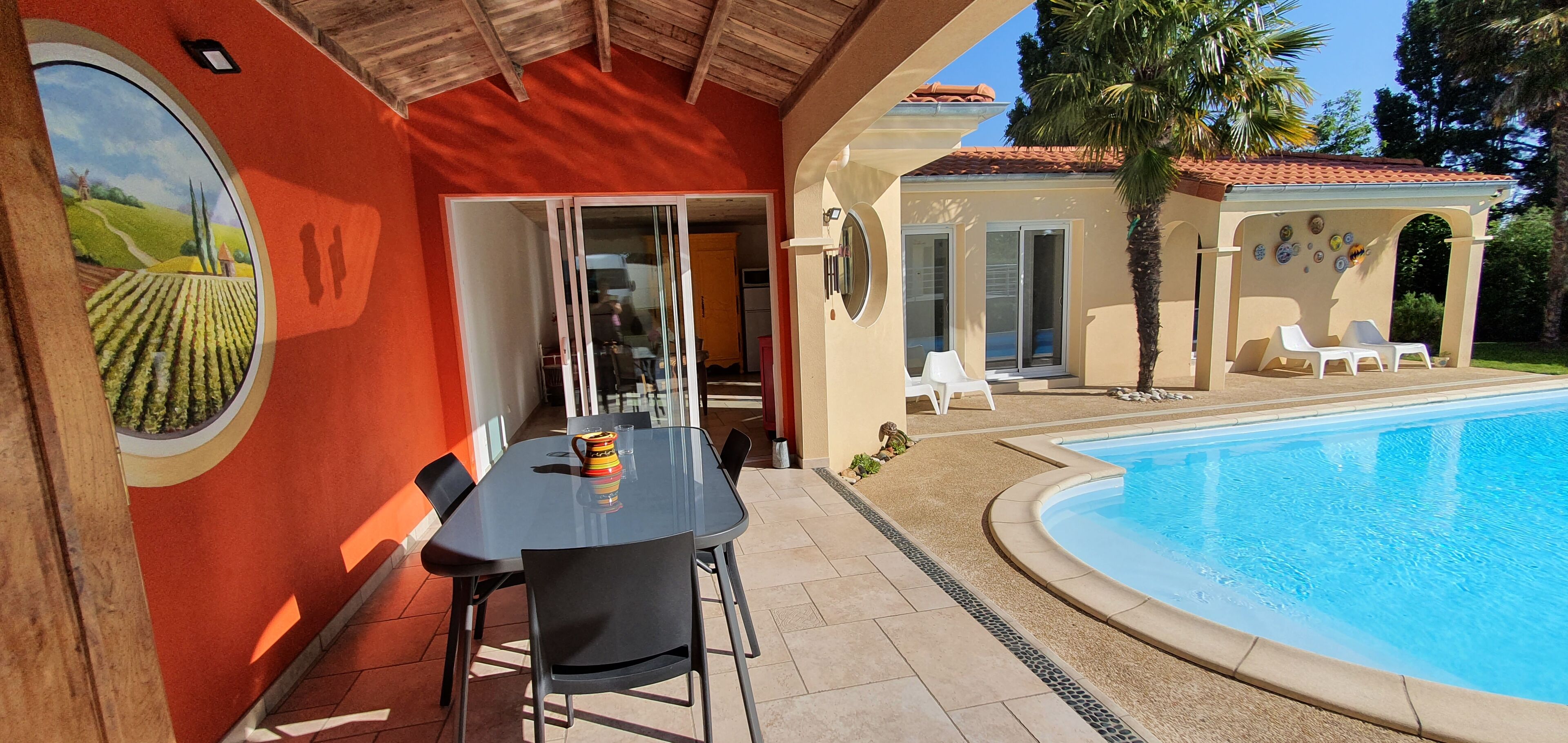 A poolside area with a table and chairs, a covered seating area with lounge chairs, and a view of a swimming pool.
