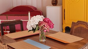 Una habitación con una mesa de madera, un florero con flores, una cama con ropa de cama roja y un armario amarillo.