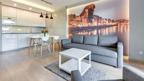 Un salon moderne avec un canapé gris, une table basse blanche et une fresque représentant un paysage urbain sur le mur.