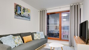 Un salon moderne avec un canapé gris, une petite table blanche et un téléviseur posé sur un meuble en bois.