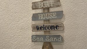Een houten bord met de tekst ‘Boat House Welcome Sea Sand’ bevestigd aan een structuurrijke muur.
