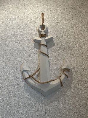 A white anchor decoration with rope tied around its shank and arms, mounted on a textured wall. - City Müllers Apartment (Bremerhaven)