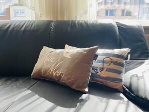 Un canapé en cuir noir agrémenté de deux coussins décoratifs, l’un sur le thème de la marine et l’autre orné d’un motif calligraphique.
