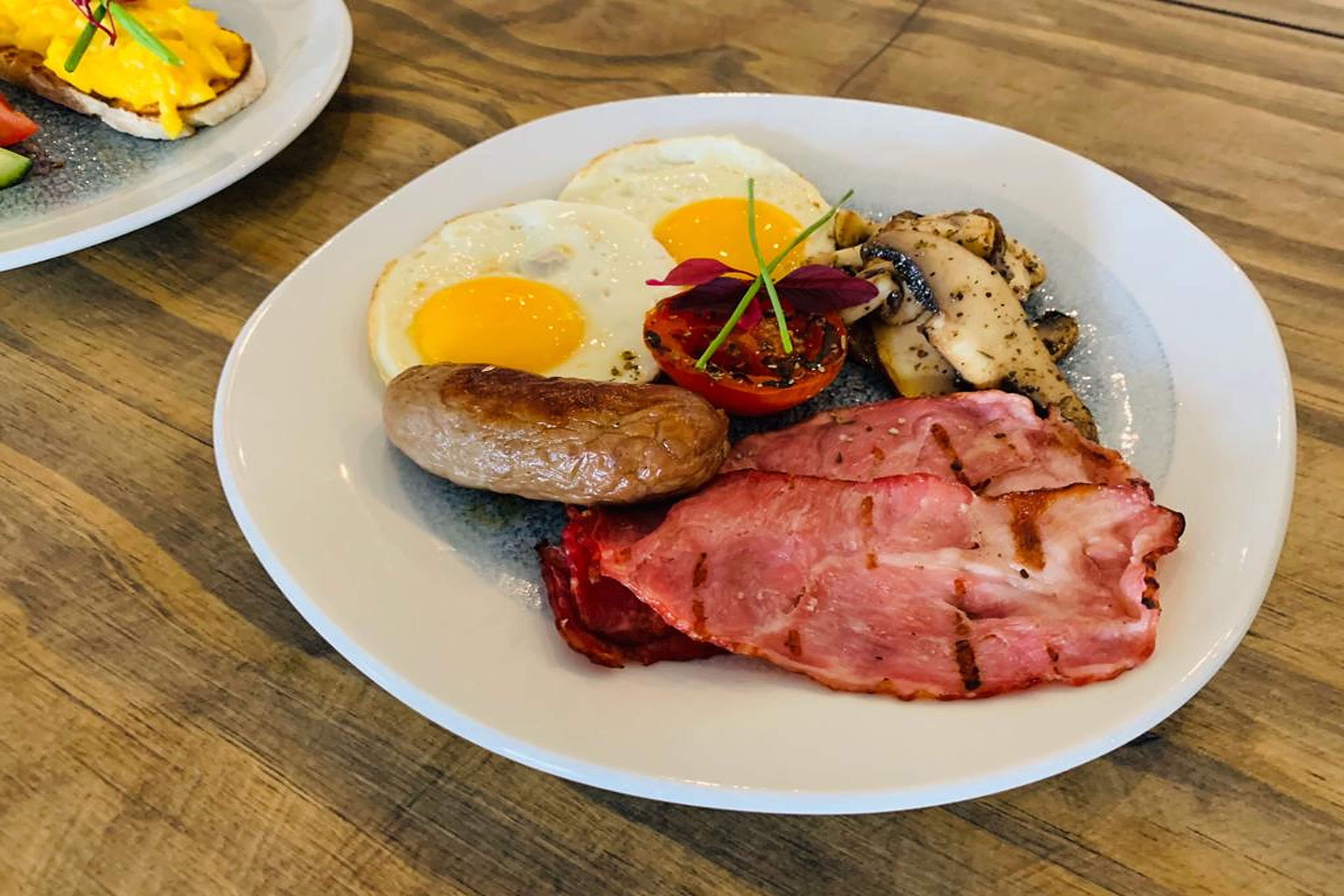 Un plato de comida para el desayuno que incluye huevos, salchicha, jamón y champiñones.