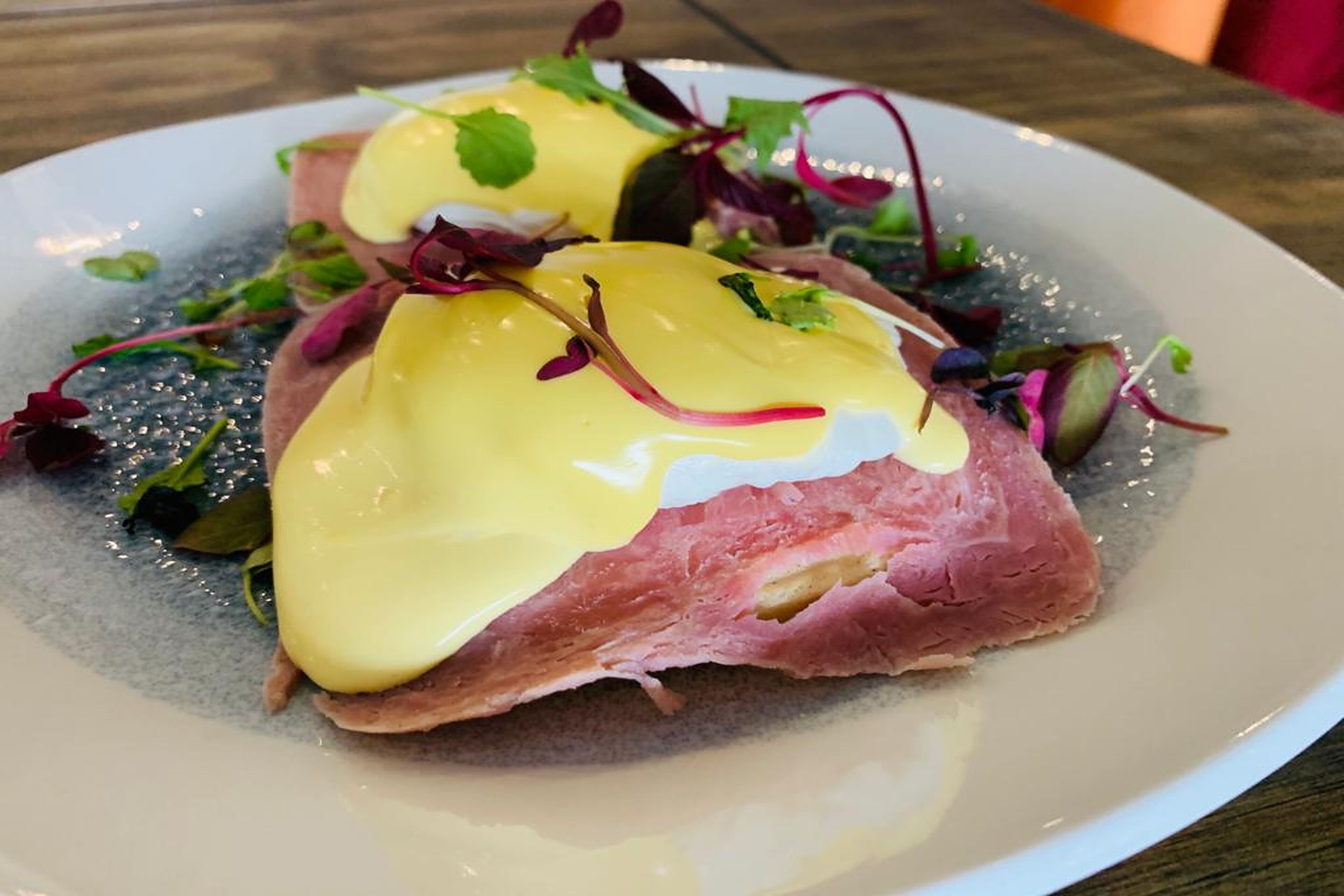 A plate with a dish that includes a slice of meat, possibly steak, topped with a yellow sauce and garnished with greens.