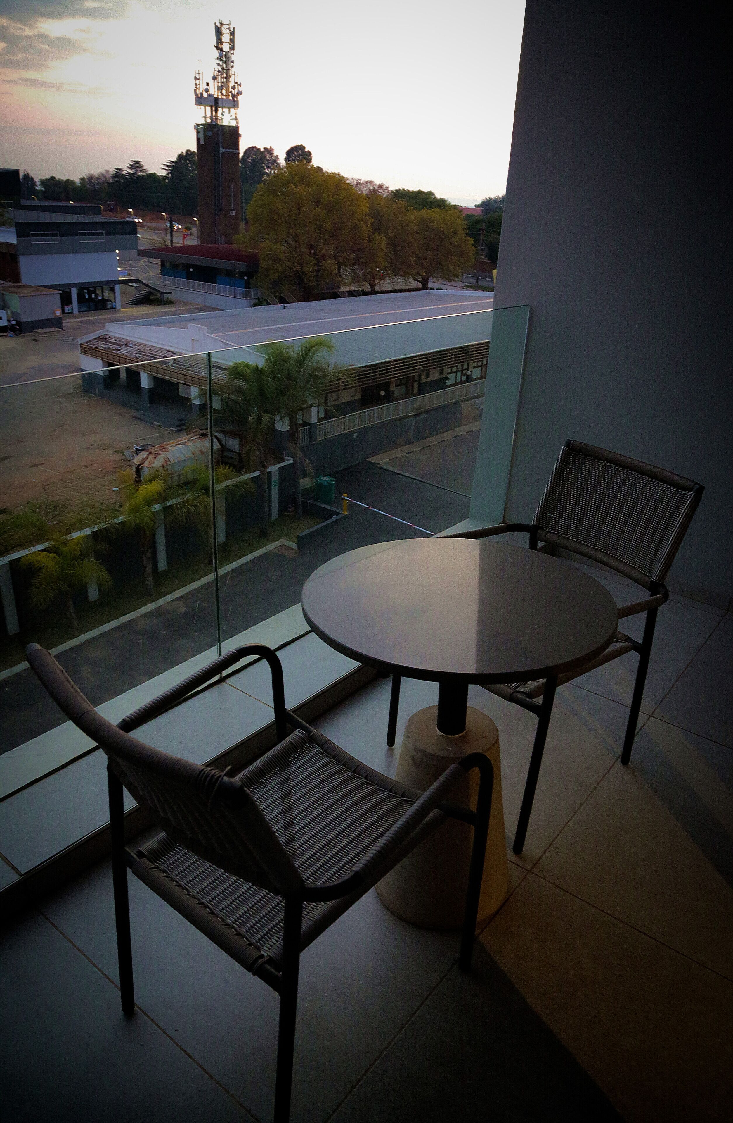 A balcony with a round table and two chairs, overlooking a street and a building with a tower.