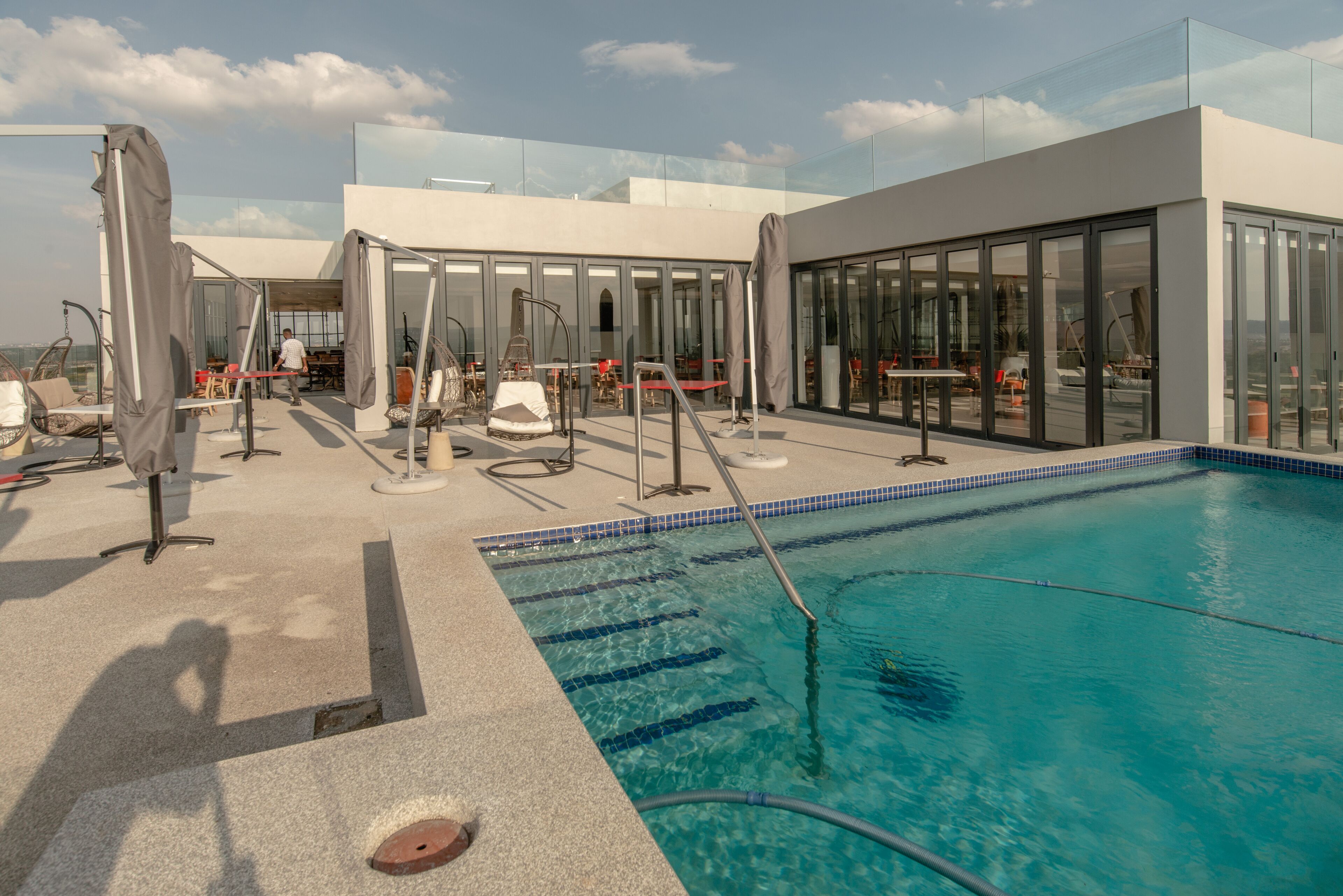 A rooftop pool area with clear blue water, glass-enclosed seating, and a modern architectural design.