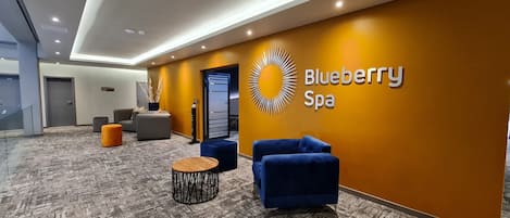 A modern spa lobby with a reception desk, seating area, and a wall sign for Blueberry Spa.