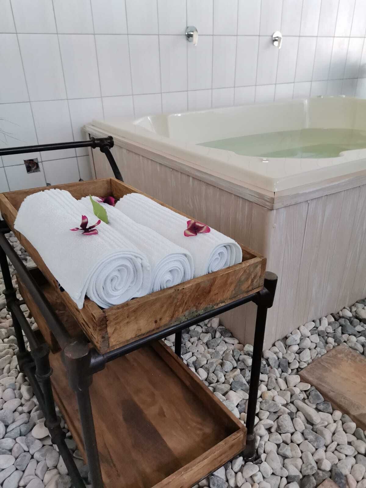 A wooden cart with towels and a flower, placed near a bathtub in a tiled room.