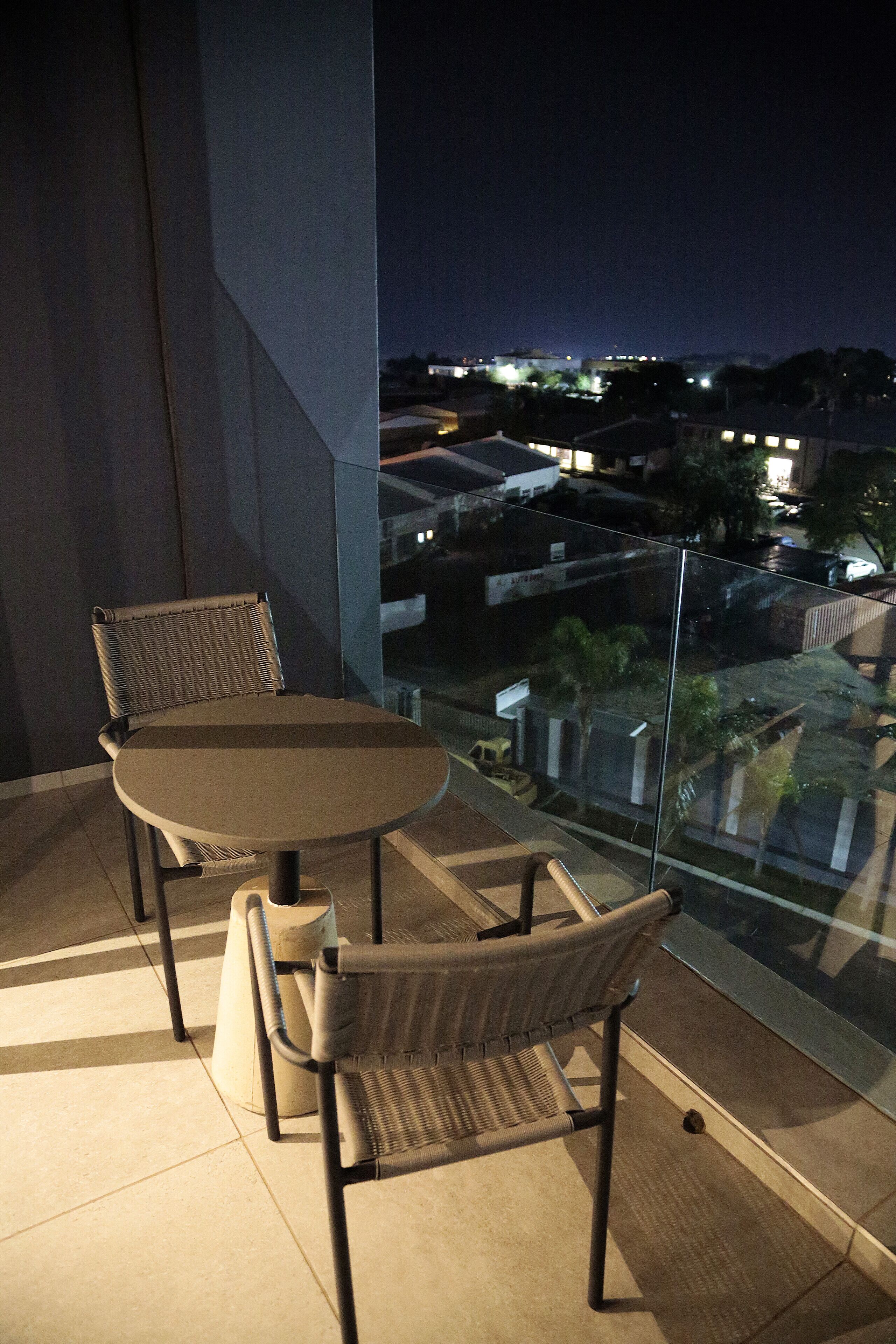Un balcon avec une table et deux chaises, donnant sur une vue panoramique de la ville la nuit.