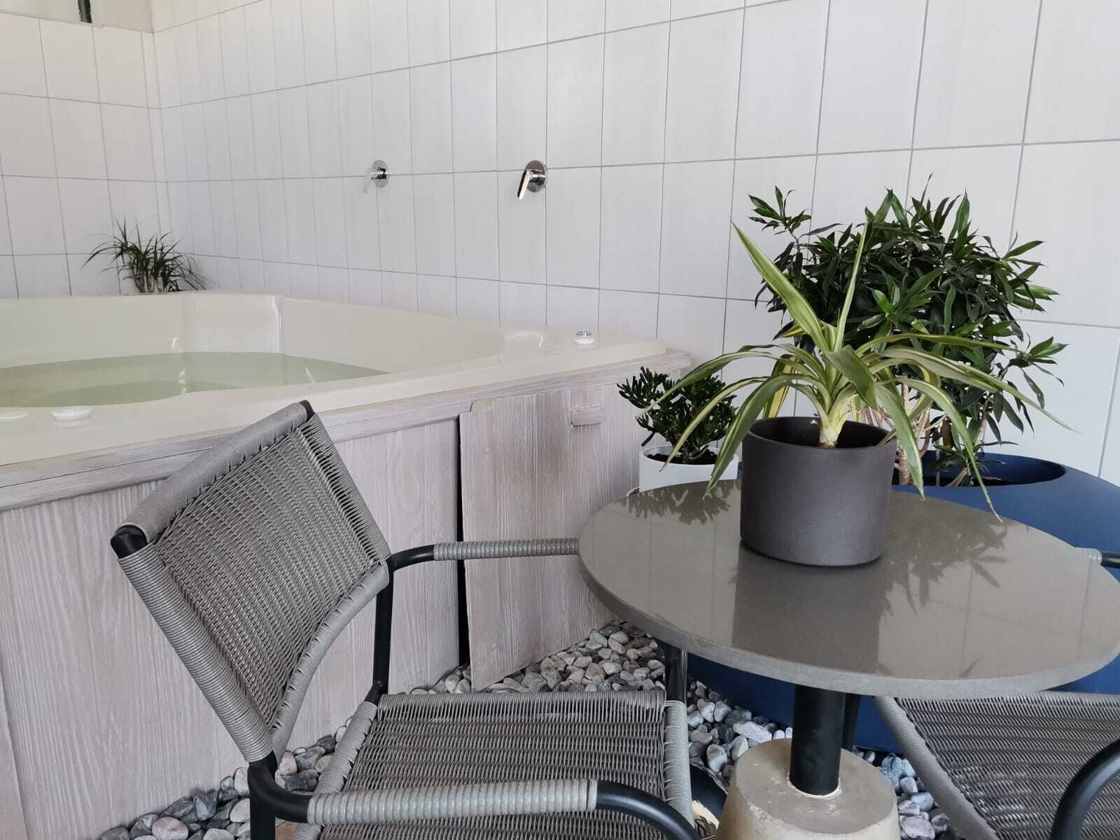 A bathroom with a bathtub, a potted plant, and a chair.