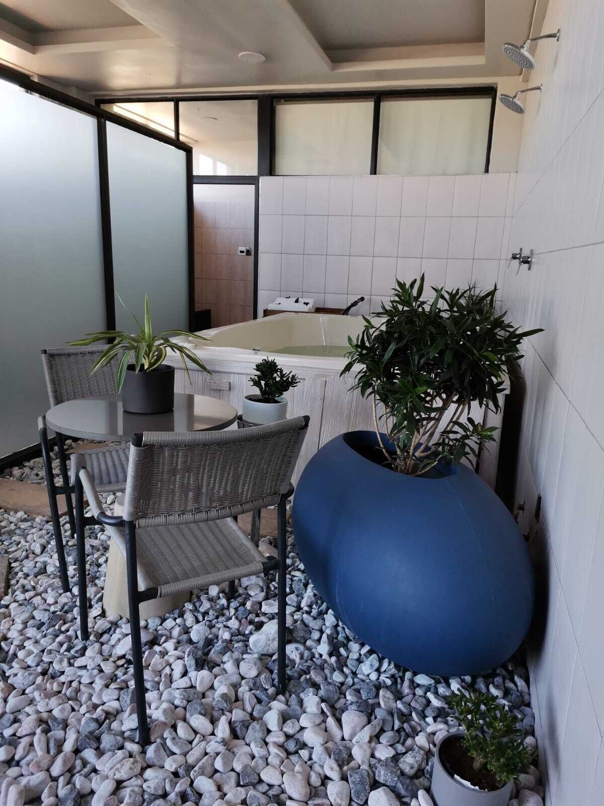 A modern bathroom with a bathtub, a shower, and a toilet. There is a small table with chairs and a potted plant.