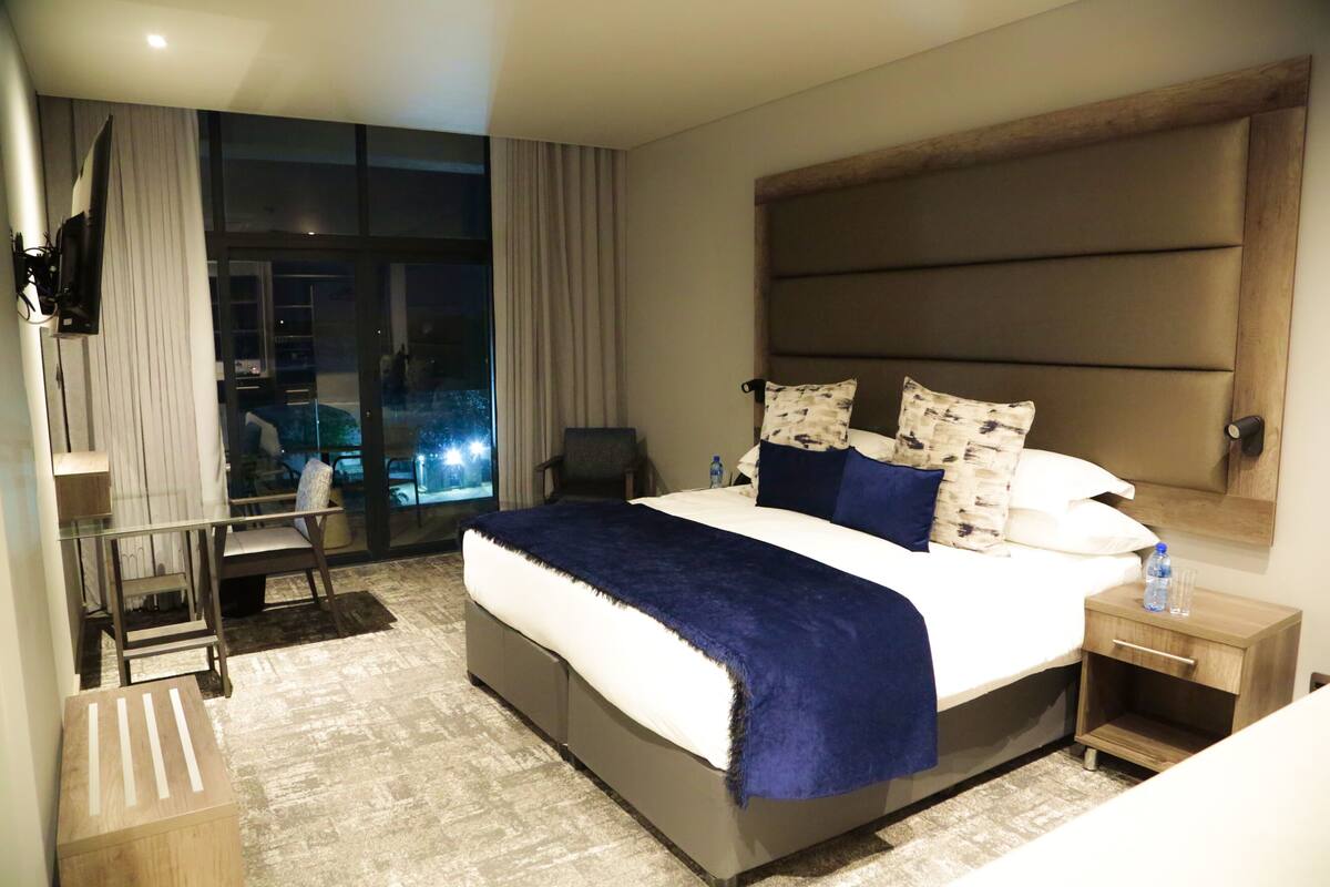 A modern hotel room with a large bed, a TV mounted on the wall, a small table, and a chair.