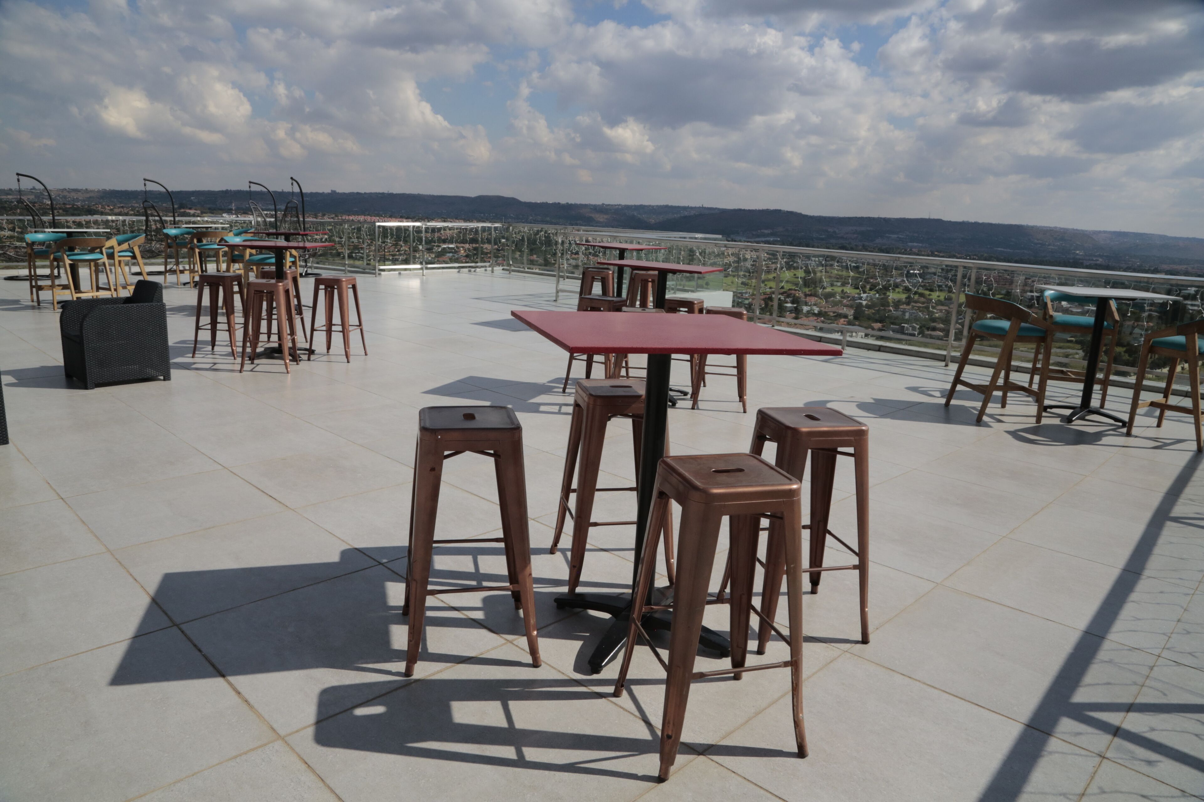 A rooftop terrace with tables and chairs, offering a view of a cityscape and distant hills.