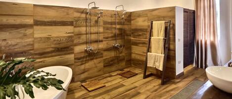 A modern bathroom with a wooden floor, a freestanding bathtub, a large sink, and a walk-in shower with three showerheads.