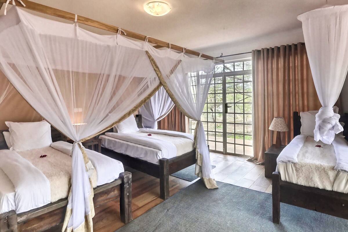 Ein Zimmer mit zwei Betten, jeweils mit Baldachin, Holzboden und Blick durch ein großes Fenster.