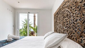 A hotel room with a bed, a decorative headboard, and a view of palm trees through a sliding door. - Luxury villa with private pool and sea view (ANCLA MAR nº5) (Roses)