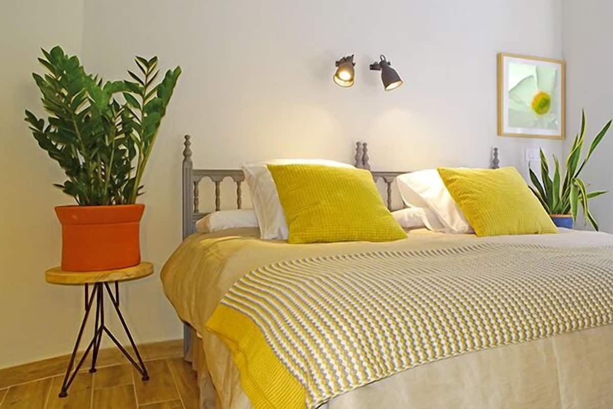 Een slaapkamer met een bed, twee bedlampen, een potplant en een lijst aan de muur.