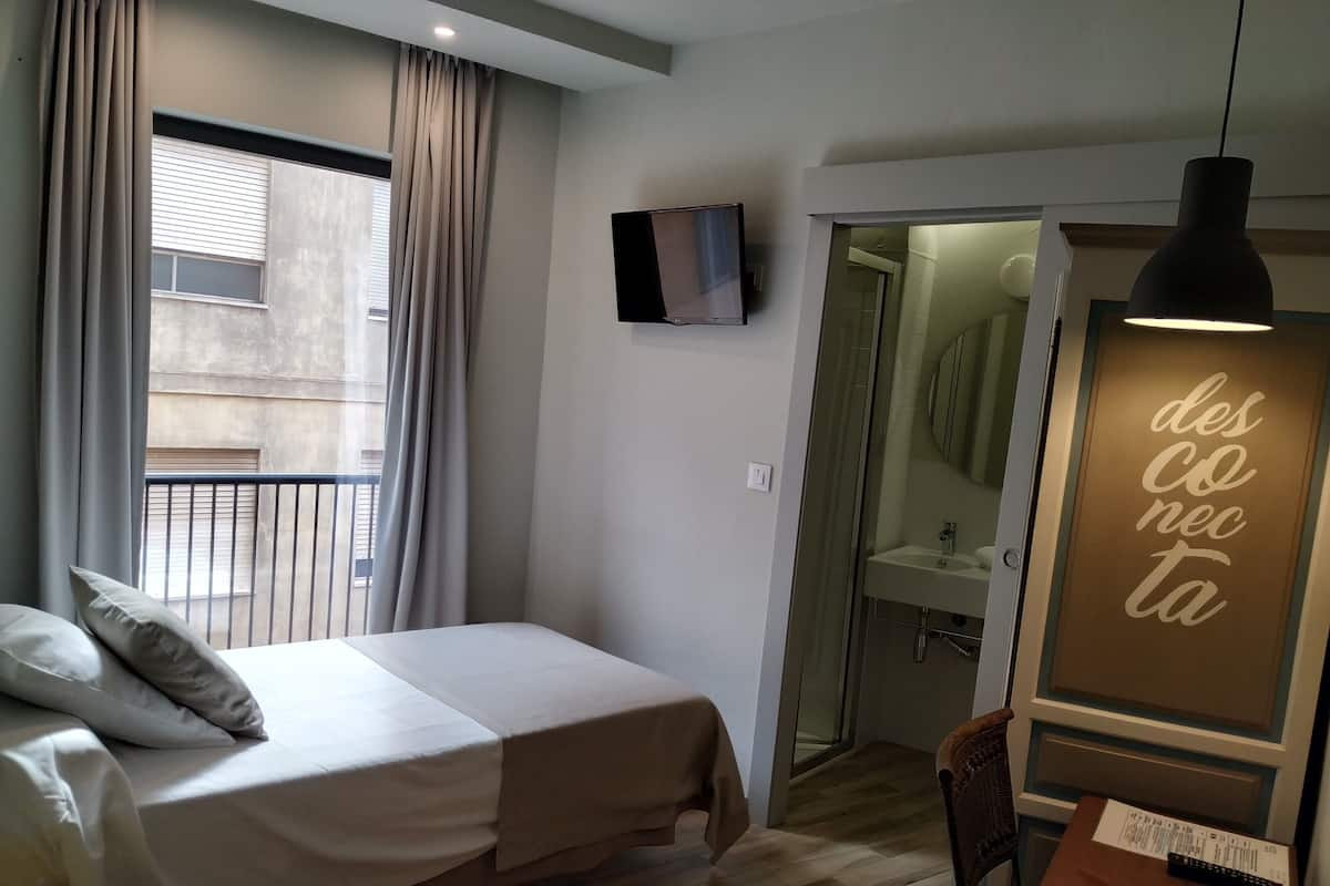 Een slaapkamer met een bed, een aan de muur bevestigde televisie, een zichtbare badkamer door een open deur en een hanglamp.