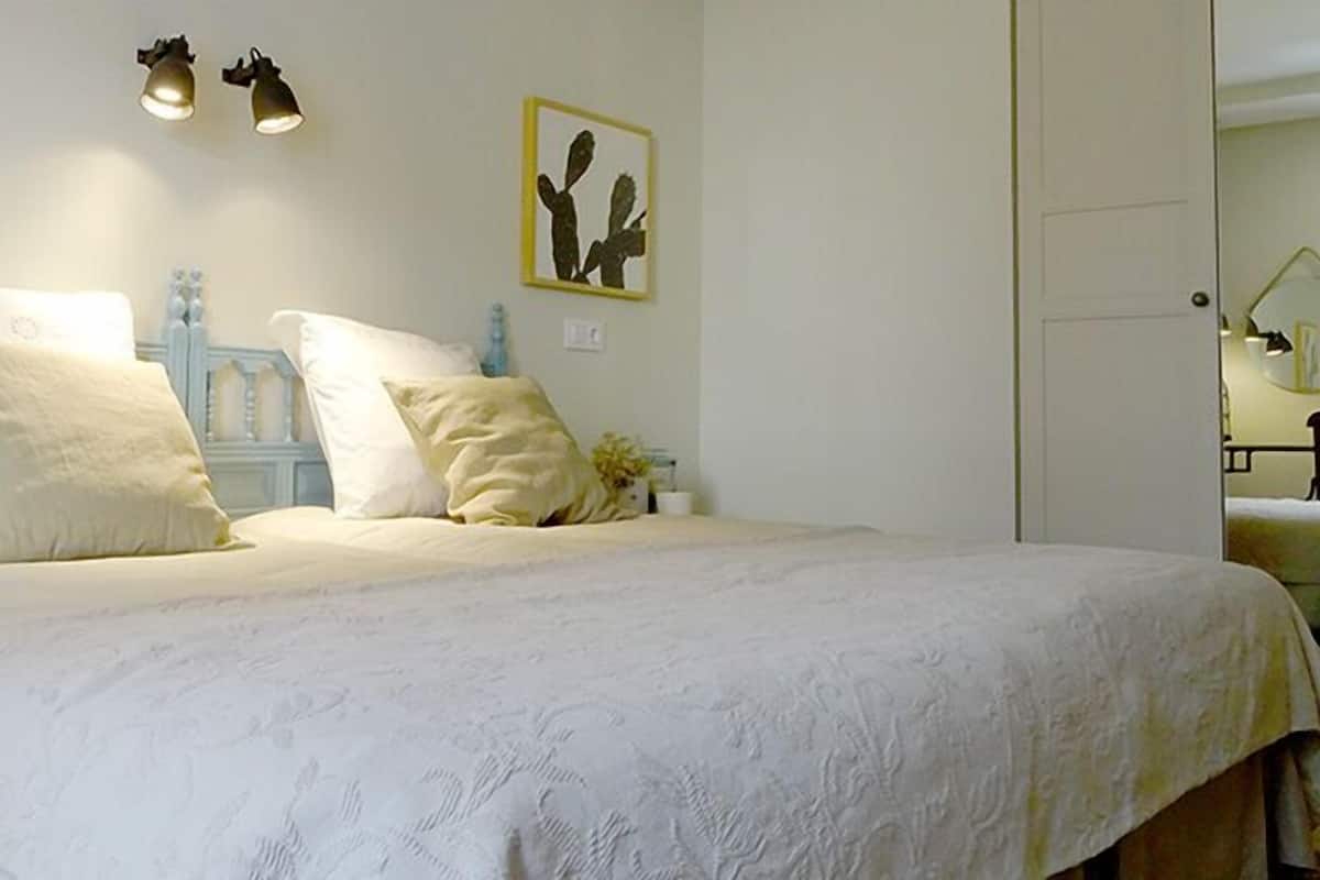 Slaapkamer met een groot bed, twee wandlampen, een ingelijst kunstwerk en een deur aan de rechterkant.