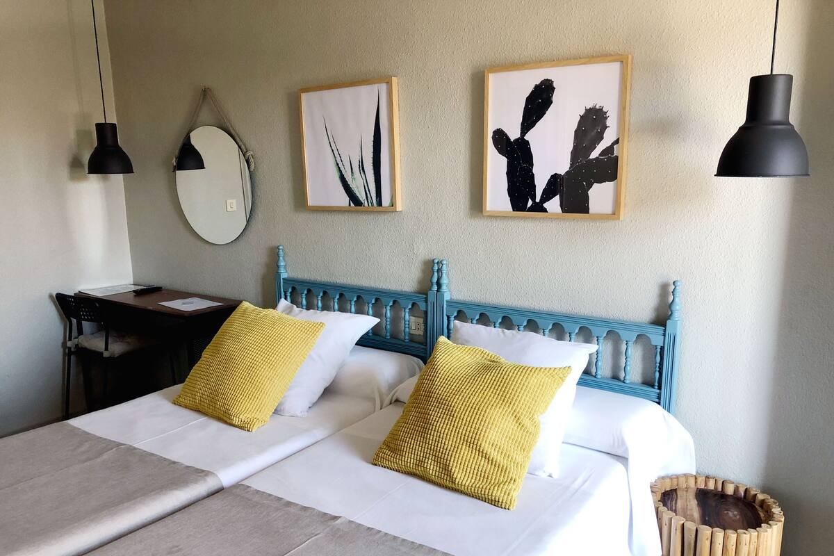 Een netjes opgemaakt bed met twee kussens, een houten hoofdbord en een nachtkastje met een lamp.