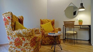 Una habitación con dos sillones de estampado floral, una mesita redonda, una silla de mimbre, un espejo circular y una lámpara colgante.