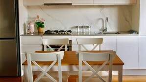 A modern kitchen with white cabinets, a stainless steel refrigerator, a wooden dining table with white chairs, and a gas stove. - McCrae beach Villa on Wattle Place, a 5 mins walk to the beach (McCrae)