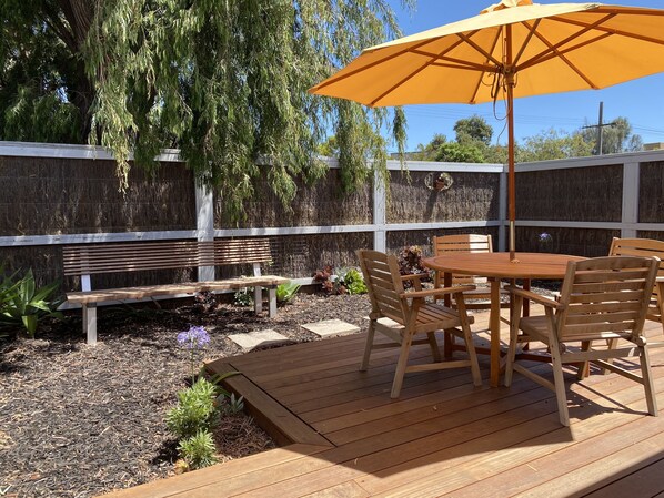 A wooden deck with a table and chairs, an umbrella, and a bench.