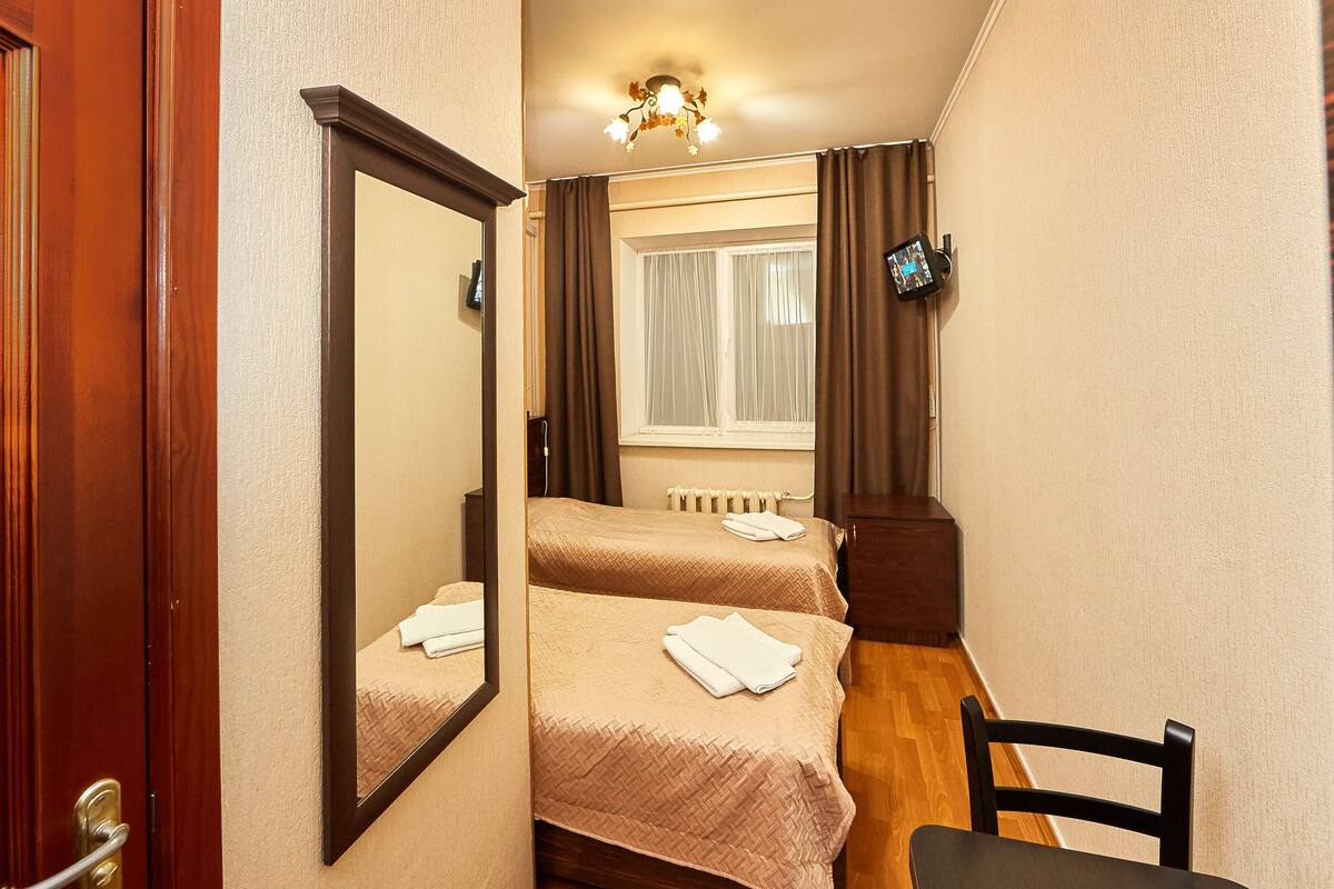 Habitación de hotel con dos camas, piso de madera, un espejo, televisor y ventana con cortinas.