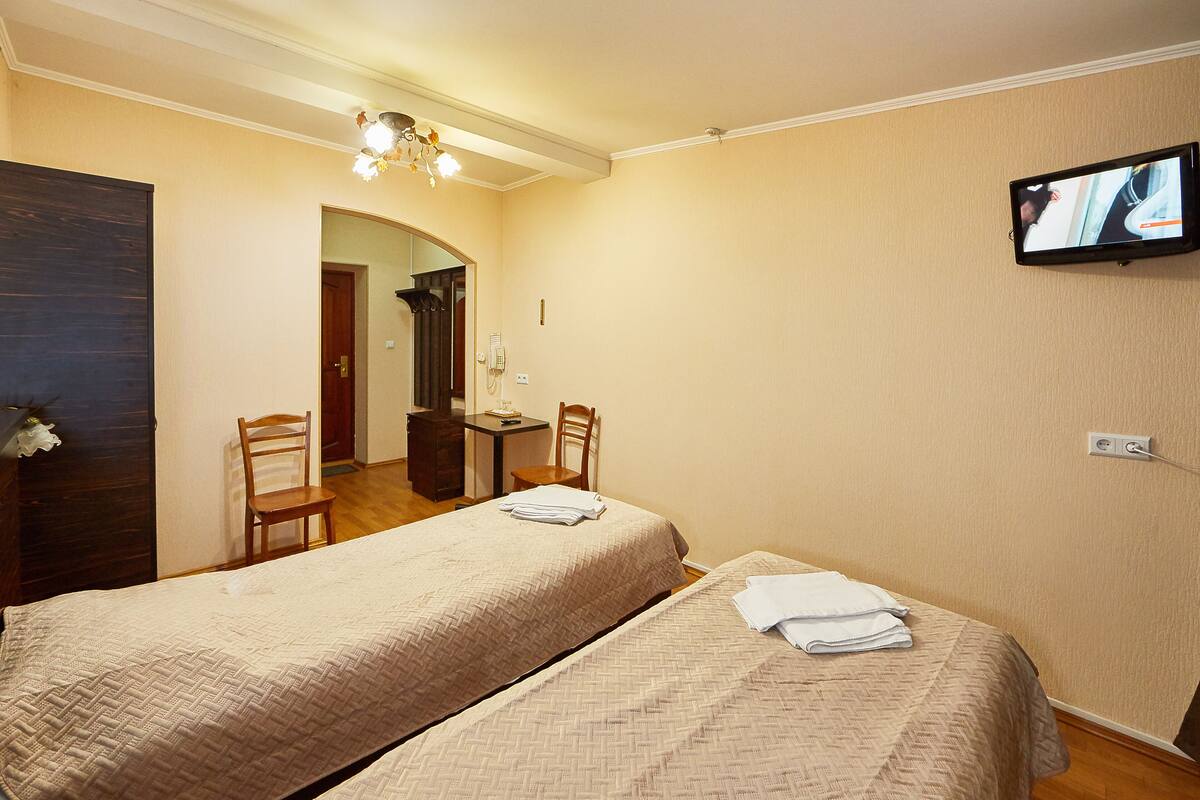 Habitación de hotel con dos camas, un televisor en la pared, un escritorio con silla y una mesita de noche con lámpara.