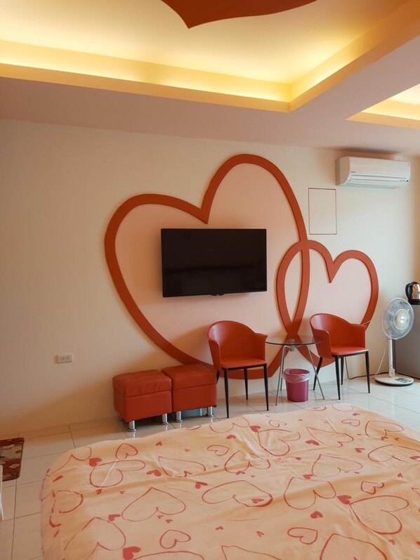 Quarto moderno com cama grande, televisão na parede e duas cadeiras vermelhas.