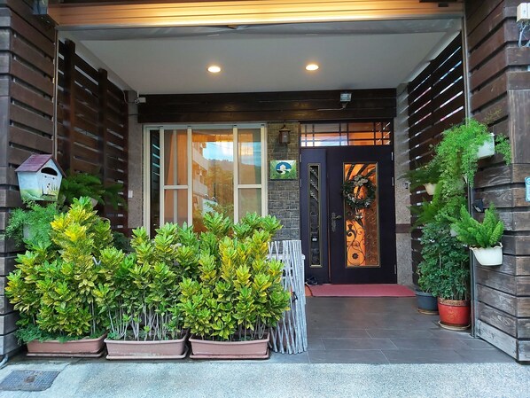 A modern building entrance with a glass door, potted plants, and a wooden fence. - Happy Heart B&B (Taitung)
