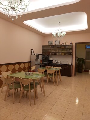 A dining area with a table and chairs, a kitchen area with appliances, and a chandelier. - Happy Heart B&B (Taitung)